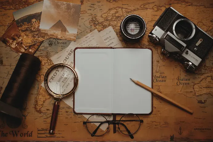 an open notebook, magnifying glass, a pen, and a pair of